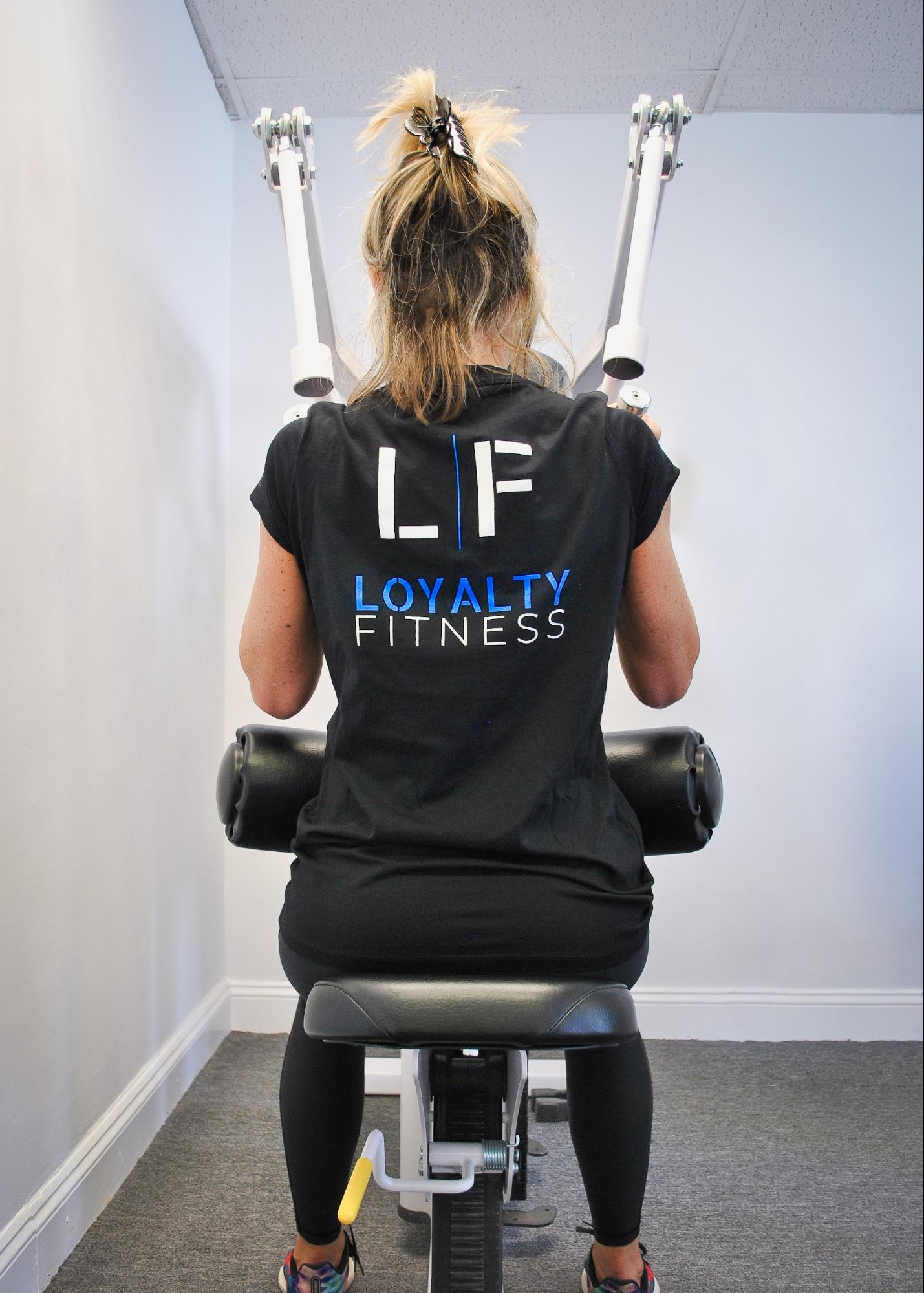 Woman wearing a shirt with the Loyalty Fitness logo on the back while working out.