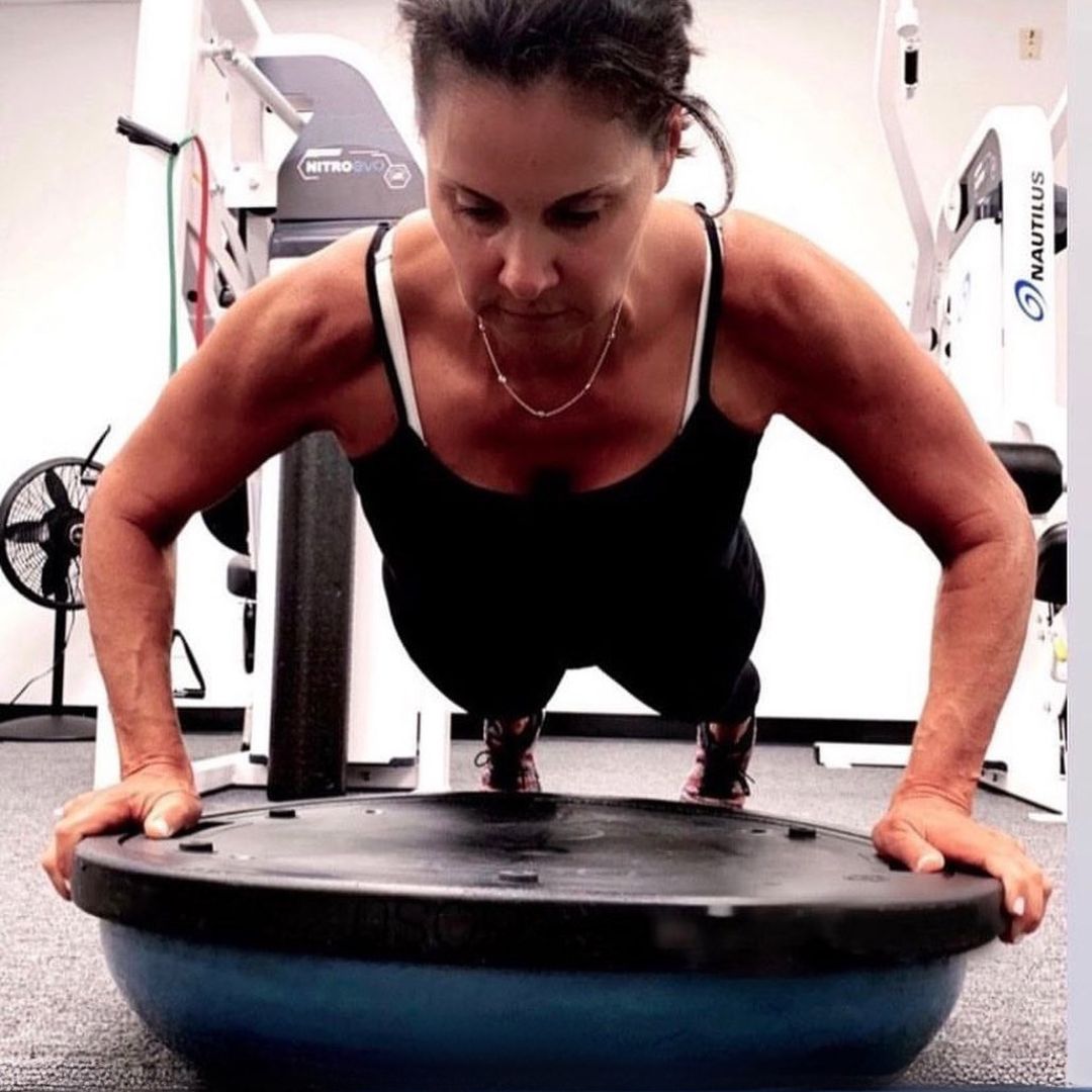 Person performing a push-up on a BOSU ball in a gym with focused determination.